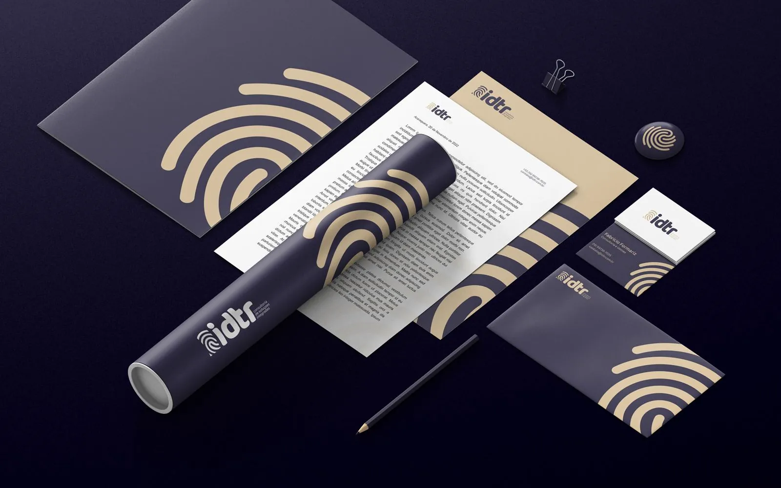 Papelaria da IDTR sobre fundo lilás escuro: pasta, papel de carta, envelope e cartões, todos com a impressão digital dourada.
