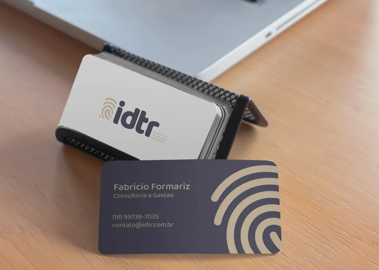 Cartões de visita da IDTR sobre uma mesa de madeira. A frente é clara com o logo, o verso é lilás com a impressão digital dourada.